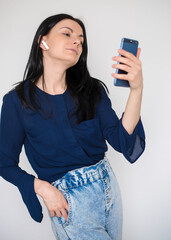 Brunette girl with bluetooth headphones makes selfie with the phone