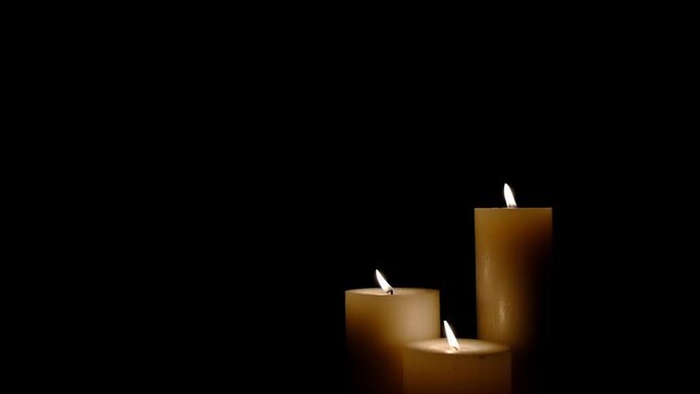 Three white burning candles blowing out. Isolated candles burning over dark background.White paraffin candles with yellow shades burns on a black background.