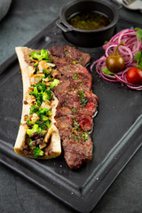 beef steak with sugar bone, served with sauce and salad of onions, pomilors and peppers. dark background