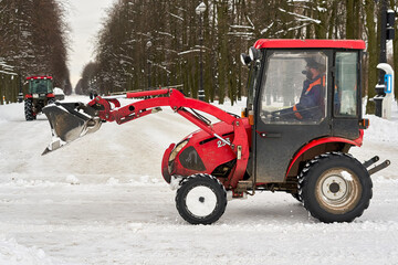 Red tractor with a large bucket removes snow in a city park