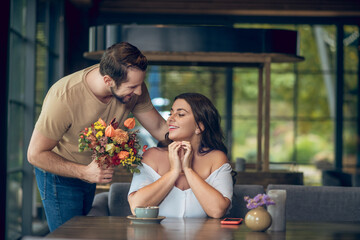 Woman sitting at table and standing man with bouquet