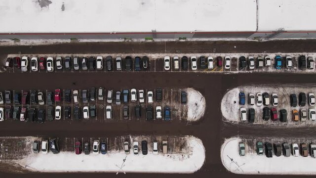 Passenger cars stand in straight rows in a parking lot in winter. Bird's eye view of a large number of cars. The vehicles are next to the mall, the owners are gone shopping.