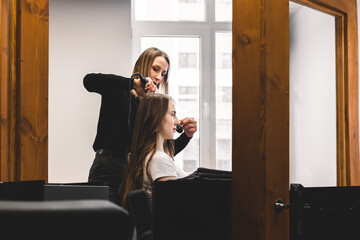 Master woman hairdresser gently curls hair curling girl in a beauty salon. Hair styling