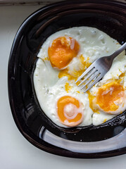 photo of fried eggs in a black plate on a white background.  food photo