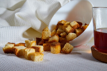 Square toasted pieces of homemade delicious rusk, hardtack, Dryasdust, zwieback on a plate and black tee in a cap on a white tablecloth.