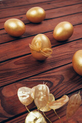 Golden colored Easter eggs with dry flowers over dark wooden planked background. Happy Easter greeting card. Vertical image.