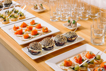 A plate of mini burgers, black buns sprinkled with white sesame seeds. There are salmon roll dishes nearby