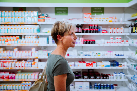 Caucasian middle-aged woman searching for flu medication walking through isles in drugstore 