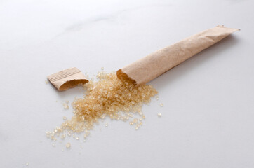 Closeup of opened kraft paper stick of brown sugar on the white table