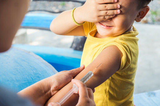 Scared little Asian boy receiving needle syringe vaccine dose from doctor at hospital. Child fear while injection treatment disease care virus. Immunity chemistry research vaccination medical concept