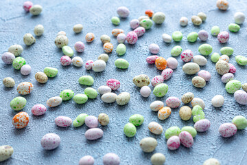 Candy, glazed chocolate Easter eggs sprinkled on a blue concrete textured background. Happy easter time. Dessert, sweets for joy, sweet-shop. Selective focus.