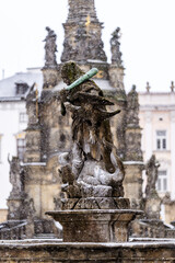 Statue of Hercules standing on a fountain in Olomouc in winter. In the background, the column of the Holy Trinity, written in UNESCO