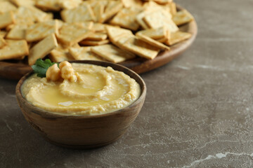 Tray with crackers and bowl of hummus on gray background