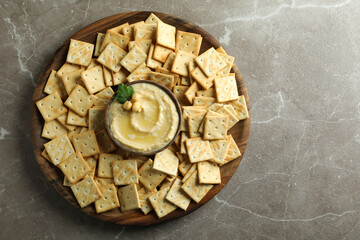 Tray with crackers and bowl of hummus on gray background