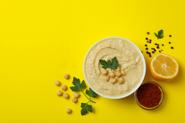 Bowl of hummus and ingredients on yellow background