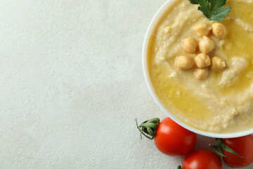 Bowl of hummus and tomatoes on white textured background