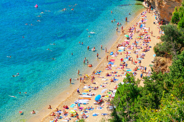 Crowd of people resting on the sandy beach . Aerial view of seaside with tourists . Famous Mogren Beach in Budva Montenegro 
