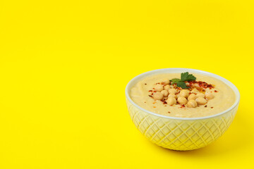 Bowl of fresh hummus on yellow background