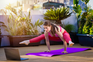 A pretty, athletic woman performs her morning pilates exercise lesson from the laptop computer...