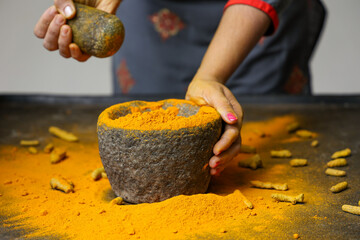 Woman hand powdering Indian spices turmeric powder stone mortar Kerala India Sri Lanka traditional Indian kitchen Masala for curry, antiseptic antiviral Ayurvedic medicine.