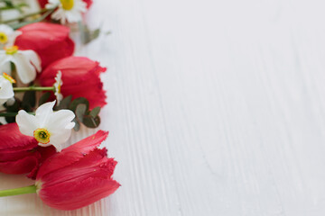Beautiful red tulips, daffodils, eucalyptus flowers border on rustic white wood.Floral greeting Card