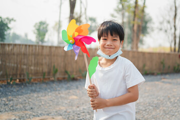 .A boy holding a toy windmill happily walking in the park and wearing a mask to protect against the...