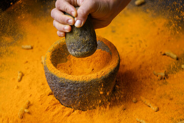 Woman hand powdering Indian spices turmeric powder stone mortar Kerala India Sri Lanka traditional...