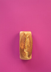 Loaf of wheat bread with golden crust on pink background. German traditional bakery and handmade tin loaf, white bread. Creative food concept, minimalism aesthetic. Fresh, daily food concept. 