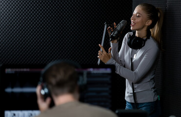 Teen female singer working in music record with male sound engineer in a voice recording studio....