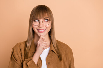Photo of minded dreamy young woman look empty space hold hand chin think isolated on beige color...