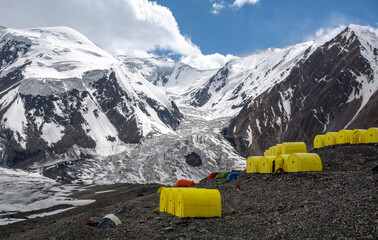 landscape with snow covered mountain range and bright camp tents under glacier moraine 