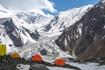 tents under high altitude mountain range with glacier coming down to