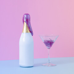 Party bottle of champagne with purple slime coming out of it beside crystal glass filled with slime. Blue table against pink wall. Creative minimal concept with purple gradient light.