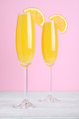 Fresh alcoholic Mimosa cocktails with orange slices on white wooden table