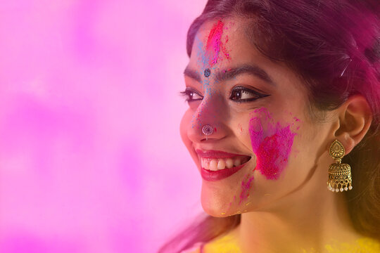 A YOUNG WOMAN WITH GULAL ON HER FACE LOOKING AWAY AND SMILING	