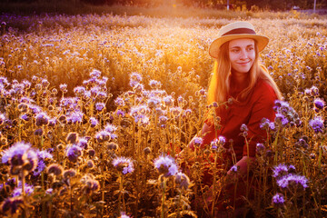 Fototapeta na wymiar Beautiful young woman in violet phacelia flowers field in sunset tima