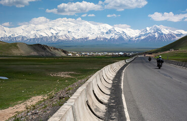 road to the high mountains range with bikers sillhouettes  on it going fast trough meadow landscape 