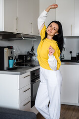 Brunette girl with bluetooth headphones dances in the kitchen in the morning and makes coffee in a coffee machine