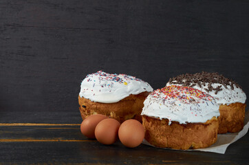 Traditional Easter bread or cake with white glaze and multicolored rainbow sprinkle decorated with eggs on the black wooden background. Close up view