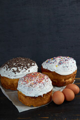Traditional Ukrainian Easter bread or cake with white glaze and multicolored rainbow sprinkle decorated with eggs on the black wooden background. Side view with copy space