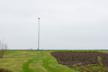 A lone light pole with grass in the foreground and a depressed day.