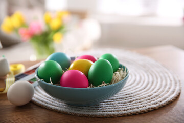 Fototapeta na wymiar Bright painted Easter eggs in bowl on wooden table indoors, space for text