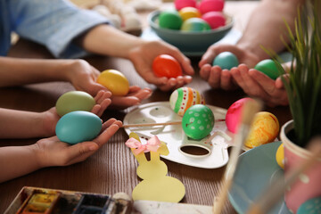 Father, mother and their child painting Easter eggs at wooden table, closeup