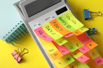 Calculator covered with stickers on yellow background, closeup. April fool's day