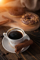 A cup of aromatic black coffee and coffee beans on the table. Morning espresso coffee for breakfast in a beautiful white cup. With a delicious donut in the background. 