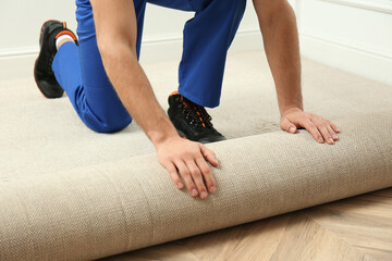 Naklejka premium Worker rolling out new carpet flooring indoors, closeup