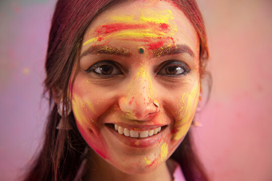 PORTRAIT OF A YOUNG WOMAN SMILING AT CAMERA WITH HOLI COLOURS ON HER FACE	