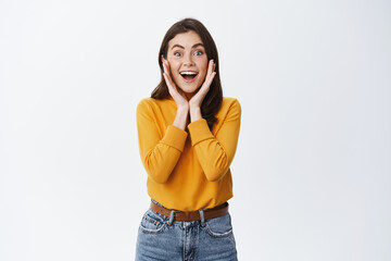 Wow amazing. Impressed young woman smiling excited, holding hands on face with natural light make...