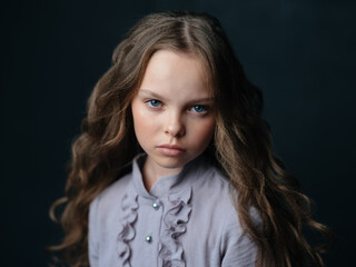 Portrait of a beautiful girl with curly hair and a gray dress on a dark background