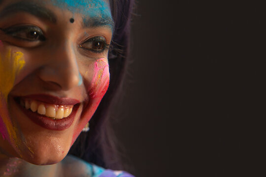 A WOMAN WITH GULAL ON HER FACE HAPPILY LOOKING AWAY 	
